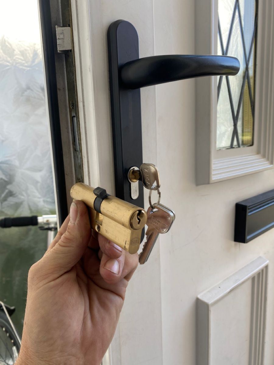 A brass euro cylinder held in front of a composite door with a black handle