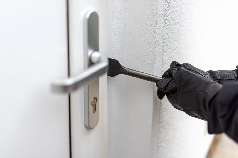 A gloved hand forcing a crowbar into the frame beside a door lock