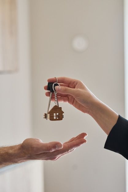 A wooden house keyring being handed from one hand to an open palm